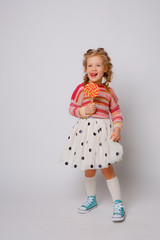 little  girl a blonde child with a Lollipop on a stick smiling in colored clothes on a white background