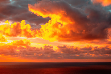 Naklejka na ściany i meble Aerial view of colorful clouds over horizon lit by sun setting into Pacific ocean at Piha beach