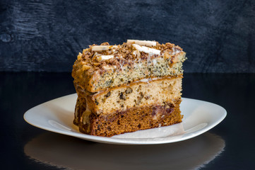 A piece of cake on a white plate reflected from the table on a dark background