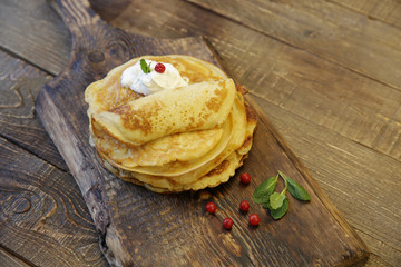 tasty pancakes with sour cream and red berries on a wooden rustic background