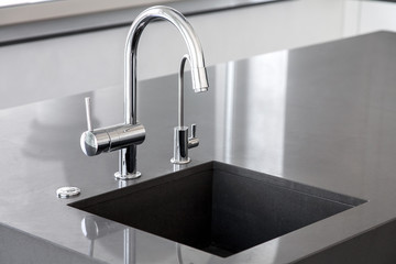 blank kitchen sink of dark gray marble with chrome tap in a clean kitchen with a glossy work...