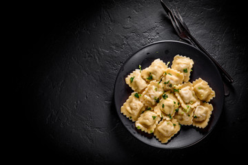 Meat dumplings - russian pelmeni, ravioli with meat in black plate on Dark grey black slate background