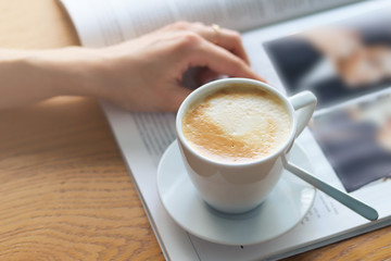 A cup of coffee in a trendy cafe, a girl reads a lcd and drinks coffee
