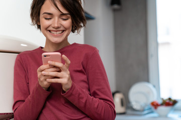 Photo of joyful young woman laughing and using smartphone