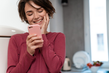 Photo of joyful young woman laughing and using smartphone