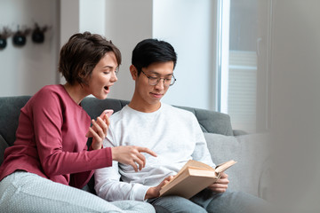 Photo of excited multinational couple reading book and using smartphone