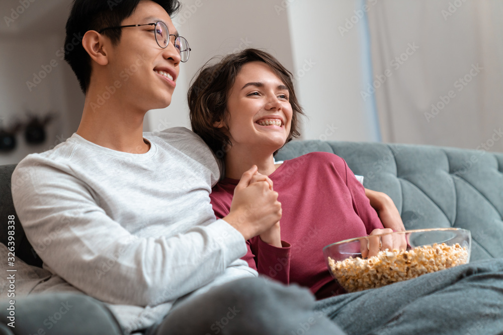 Poster Photo of joyful multinational couple eating popcorn and watching movie