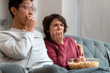 Photo of shocked multinational couple eating popcorn and watching movie