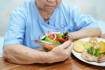 Asian senior or elderly old lady woman patient eating breakfast vegetable healthy food with hope and happy while sitting and hungry on bed in hospital.