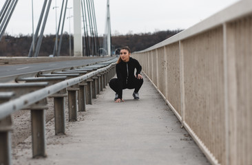 Young woman in black sports outfit resting after running on the bridge in the city.