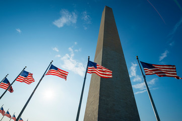 Backlit view of American flags surrounding the Washington Monument in bright summer sun in Washington, DC, USA