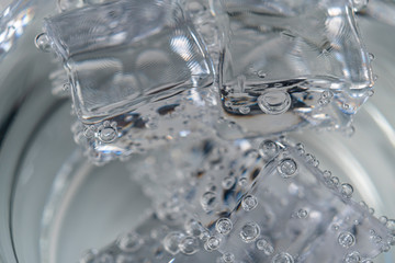 A pile of ice cubes with bubbles in a glass with pure mineral sparkling water. Natural drinks for refreshment. Macro shot.