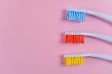 Three colored toothbrushes on a pink background. Red, yellow, blue. Copyspace. Bright tool for dental hygiene