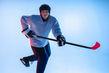 Youth. Young male hockey player with the stick on white background in neon light. Sportsman wearing equipment and helmet practicing. Concept of sport, healthy lifestyle, motion, movement, action.