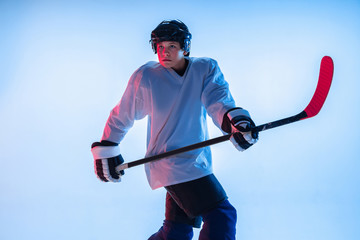 Youth. Young male hockey player with the stick on white background in neon light. Sportsman wearing equipment and helmet practicing. Concept of sport, healthy lifestyle, motion, movement, action.