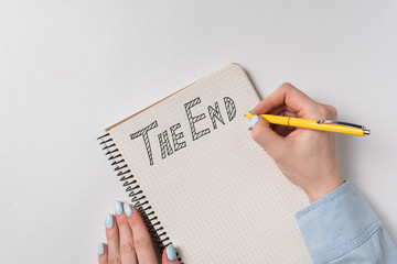 Handwritten note The end. Female hand writing text in Notepad. White background top view