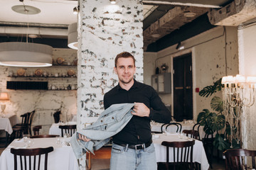 a young man in a black shirt and denim jacket walks in a restaurant