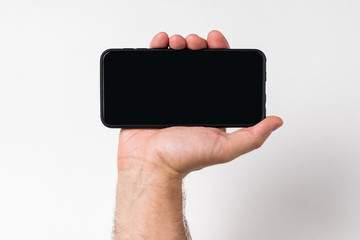 Male hand holding smartphone. White background, blank black screen. Copy space