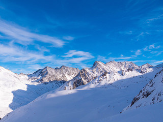 Fototapeta na wymiar Alpine Winterlandschaft mit felsdurchsetzen Bergflanken und dunkelblauem Himmel mit Schleierwolken