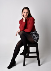 full length portrait of a pretty brunette girl wearing a red shirt and plaid skirt with leggings...