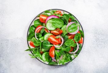 Spring vegan salad with spinach, cherry tomatoes, corn salad, baby spinach, cucumber and red onion. Healthy food concept. Gray stone table. Top view. Copy space