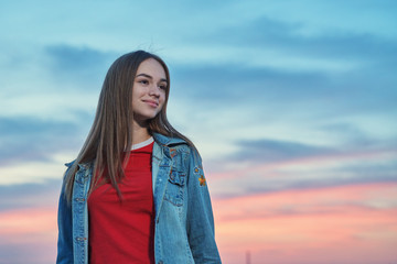 Casual teen girl standing looking away at sunset background