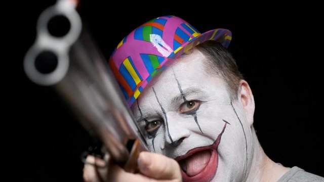 Clown man with grin on his face with shotgun in his hands close-up on black background.