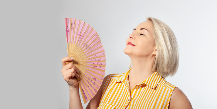 Attractive middle aged woman relaxing with fan. Mature woman experiencing hot flush from menopause isolated - Powered by Adobe