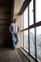 Portrait of an athletic courageous man at a large window indoors.