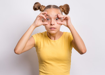 Silly teen girl making grimace - funny shocked face. Surprised child with big eyes, on grey background. Emotional portrait of amazed teenager looking at camera. Emotions and signs.