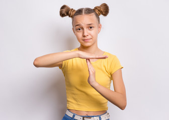 Emotional portrait of teen girl making timeout gesture, on grey background. Serious child tired and bored looking at camera and showing pause or time out sign. Student asking for time-out.