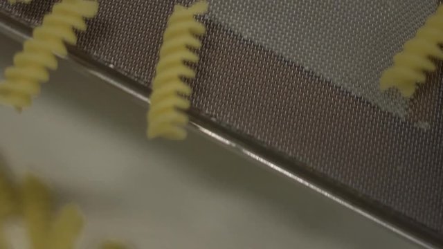 Suggestive slow moton of dried raw pasta rotini fudilli passing on a conveyor belt in a pasta factory. Italian food and gastronomic traditions.