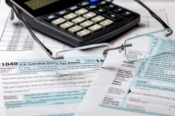 1040 income tax form 2019 with calculator and focus through glasses. Concept of filing taxes, payment, refund, and April 15, 2020 tax deadline