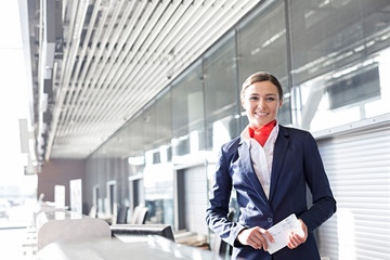 Portrait of young attractive passenger service agent holding boarding pass in airport check in area