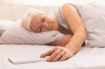 Tired senior woman in bed checking time on her phone