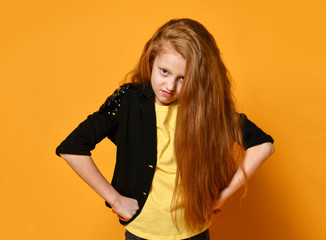 Teenage kid in black jacket and yellow t-shirt. She is looking pissed off, hands on hips, posing on orange background. Close up