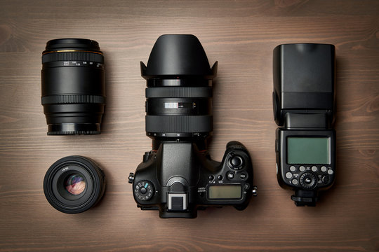 top view of modern digital camera equipment - DSLR with attached zoom lens and hood, lenses and external flashlight on wooden table