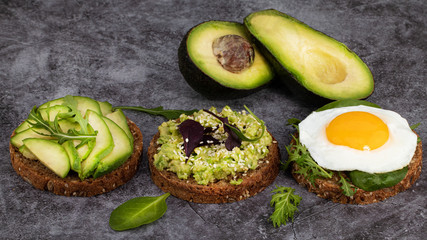 Avocado sandwich on dark rye bread with spinach and fried egg on a dark background