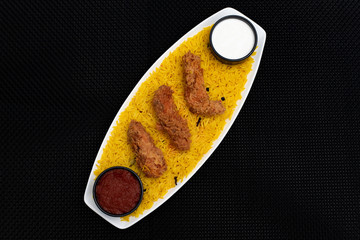 Yellow rice and fried chicken strips in a bowl with black background