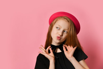 Red-headed teenager in black dress and red hat. She kissing you, holding on to choker, posing on pink studio background. Close up