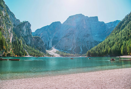 Free space for inscription text poster backdrop of Italian lake of Braies boats float on emerald water Alps in sunlight green forest on side mountains tourists relax fantastic nature. Photo wallpaper