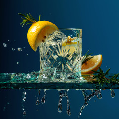 Cocktail gin-tonic with lemon and rosemary on a glass table.