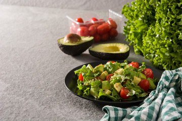 Salad with avocado, lettuce, tomato and flax seeds on black plate. Copy space