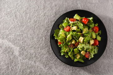 Salad with avocado, lettuce, tomato and flax seeds on black plate. Top view. Copy space