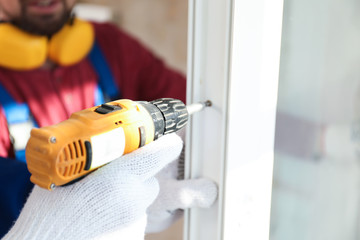 Workers using electric screwdriver for window installation indoors, closeup