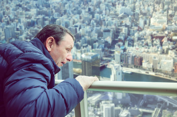 A man experiences acrophobia symptoms being on the viewing platform above a big city. He looks down with fear.  - obrazy, fototapety, plakaty