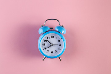 Blue vintage alarm clock on light pink color background. Alarm clock with place for text. Time...