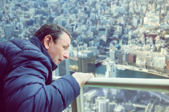 A man experiences acrophobia symptoms being on the viewing platform above a big city. He looks down with fear. 