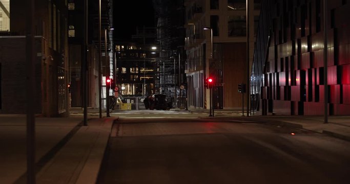 Slow motion wide shot with parallax camera movement of red public transport bus and private cars driving in illuminated intersection at night in Barcode residential quarter of Bj&oslash;rvika, Oslo Norway.