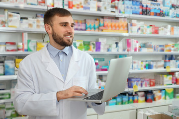 Fototapeta premium Professional pharmacist with laptop in modern drugstore
